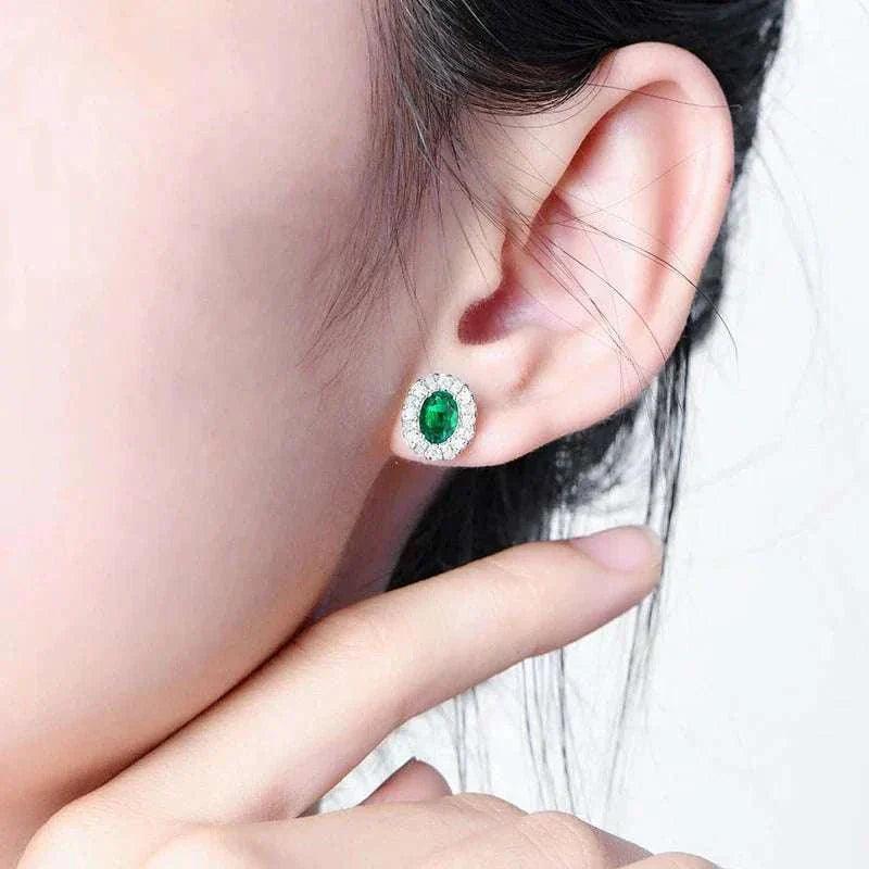 Elegant 925 silver emerald stud earrings worn on ear, showcasing a brilliant oval-cut emerald.