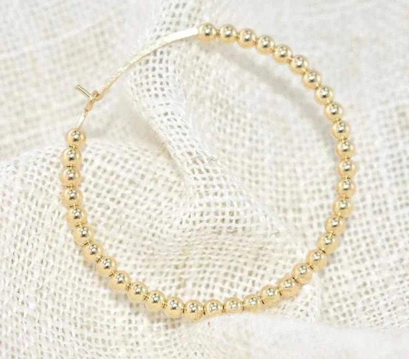 14K gold-filled hoop earring on textured fabric background.