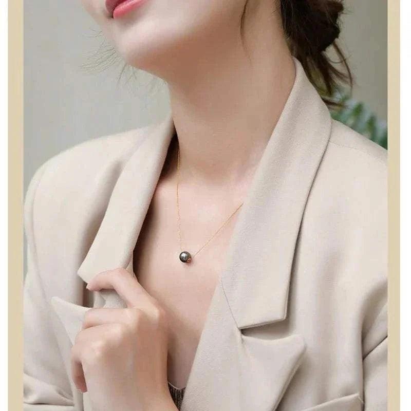 18k gold Tahitian black pearl pendant necklace displayed on person wearing a beige jacket.