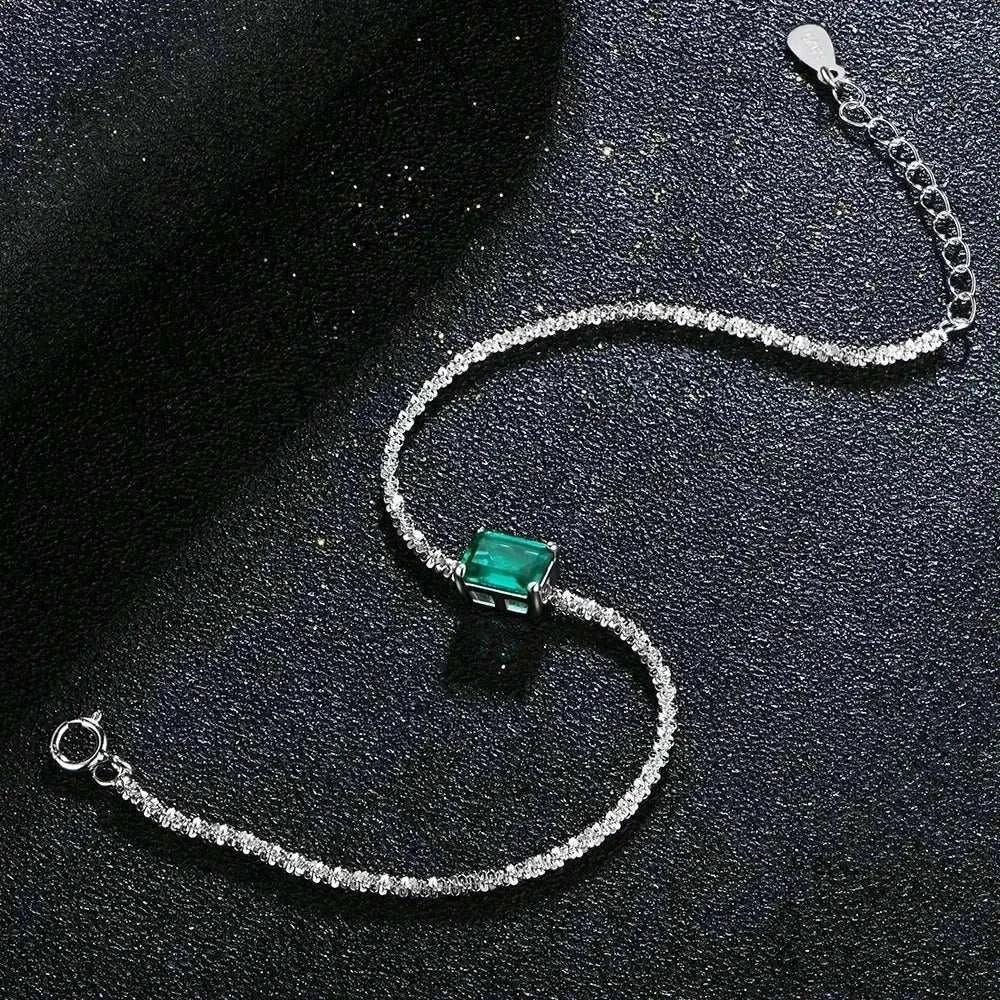Elegant 925 silver bangle with emerald and moissanite gemstones on a black surface.
